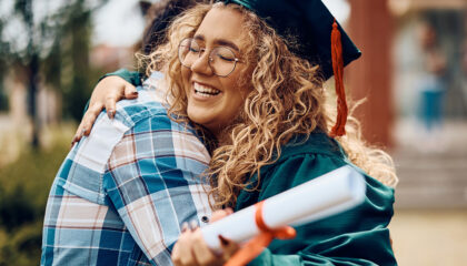 Joyful graduate hugging a loved one, holding a diploma.
